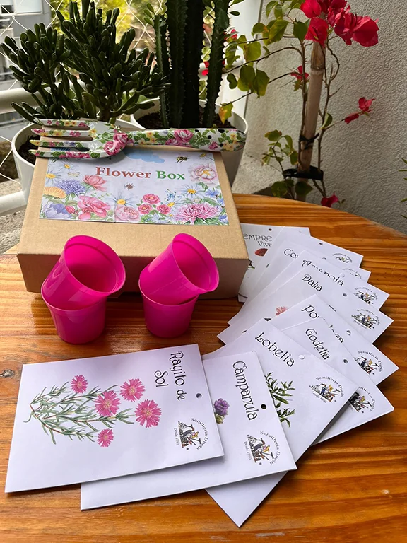 caja flower box con varios sobres de semillas macetitas rosa y herramientas floradas